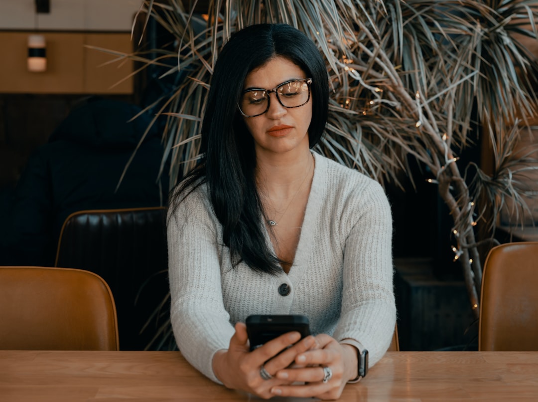 woman in white sweater sitting on chair holding smartphone