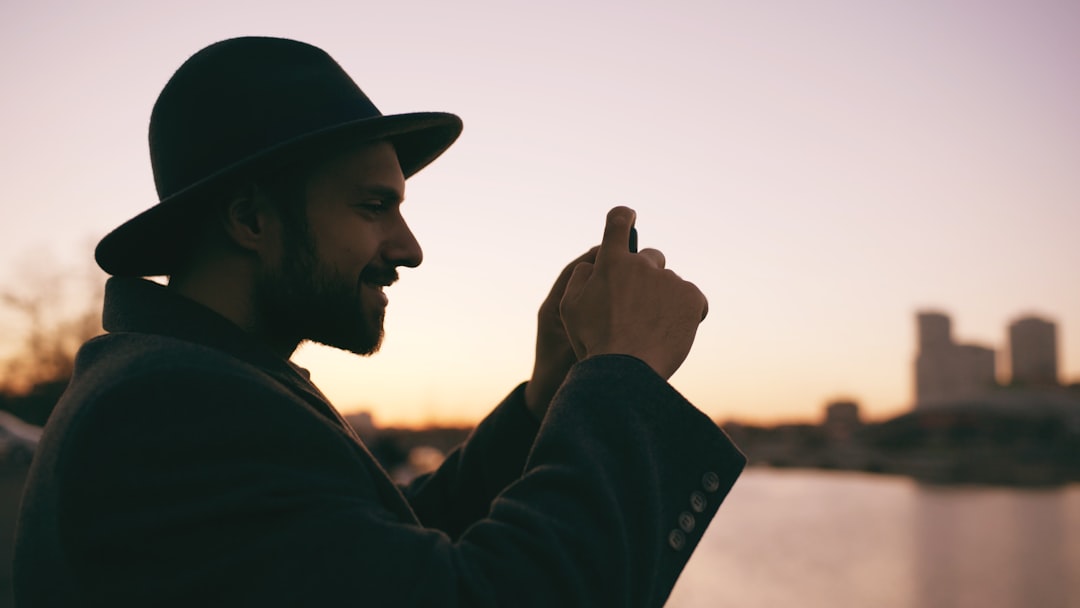 Man in hat taking photo at sunset with city skyline